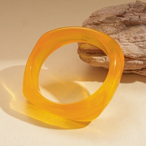Close-up of a glossy yellow resin thick wave bangle on a natural stone background