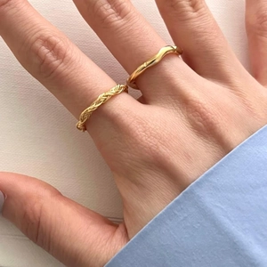 Detail of stacked gold woven knot and minimalist wave rings on a hand close-up view