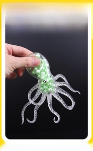 Detailed close-up showing hand squeezing a clear octopus TPR stress ball with green beads