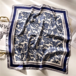 Detail of silk square scarf featuring dark blue paisley patterns and satin texture