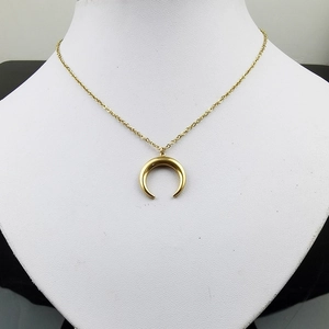 Collier avec pendentif corne dorée polie sur un support de buste blanc