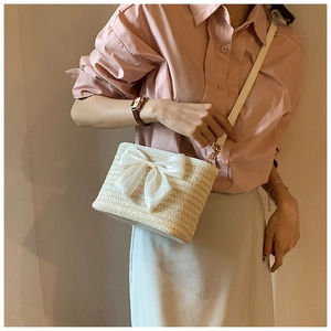 Detailed side view of woven straw bucket bag with a large white satin bow and leather strap