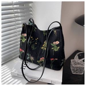 Detail of floral embroidery on a black canvas bucket bag with slim shoulder strap