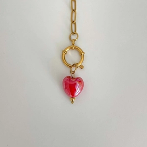 Detail view of a gold-tone necklace featuring a red heart pendant and T-bar toggle clasp