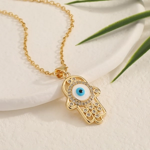 Golden Hamsa Hand necklace with Evil Eye pendant and white rhinestones on white marble