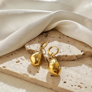 Golden irregular teardrop earrings with sparkling zircon on textured stone surface