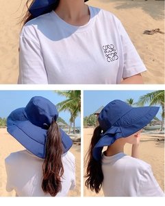 Detail van blauwe zonnehoed met paardenstaartgat en wit shirt op een zonnig strand