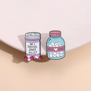 Makro-Detail von Emaille-Medizinflaschen-Pins mit AM I TAKING CRAZY PILLS und TAKE CARE Text