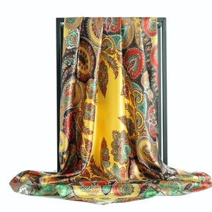 Luxurious yellow paisley satin silk scarf elegantly draped on a minimal black display stand