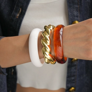 Detail of layered gold croissant, white resin, and amber tortoise shell bangle bracelets