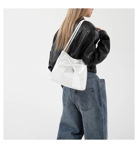 Weiße Shopper-Tasche mit großer Schleife, getragen als Schultertasche zur Lederjacke