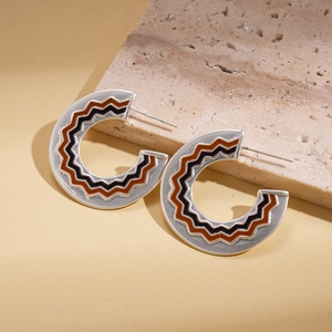 Detailed view of silver C-shaped wavy earrings with brown and black oil drip patterns