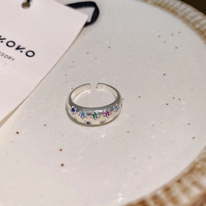 Detail of silver open ring featuring colorful star-shaped stones on white ceramic