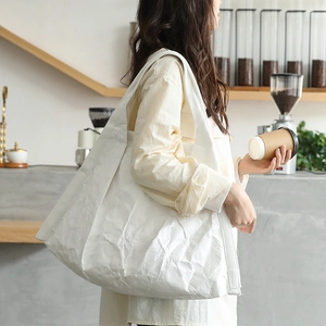 White oversized pleated shoulder bag with unique paper-like texture in a casual cafe setting
