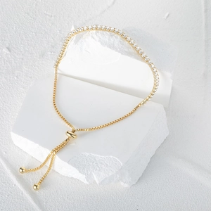 Detail of adjustable gold tennis bracelet with clear zircons on white stone texture