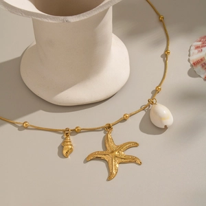 Close-up of gold starfish pendant with natural shell on a minimalist ceramic setting