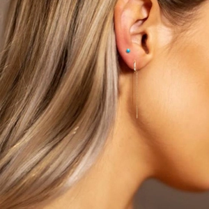 Detail of gold tassel chain earring and turquoise stud worn on the earlobe