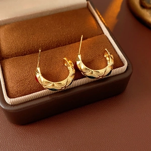 Detailed macro view of vintage gold diamond-patterned hoop earrings in a brown velvet box