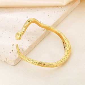 Nahaufnahme des goldenen Schlangenarmbands mit detaillierter Schuppenstruktur auf Stein