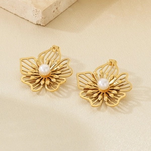 Close-up of hollow gold flower earrings with a central pearl on a stone base