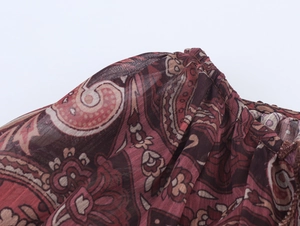 Detail von rotbraunem Paisley-Druck auf leichtem Chiffonstoff mit Rüschen und Nähten