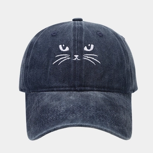 Close-up detail of white cat embroidery on washed denim blue baseball cap fabric