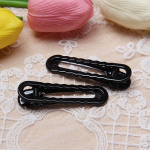 Macro shot of two glossy black wavy hair clips on a white lace background with tulips