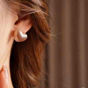 Gros plan de boucles d'oreilles cœur en résine beige mat portées par un mannequin chic