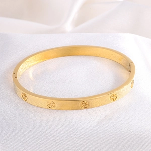 Close-up of gold stainless steel bangle with radial patterns on white silk fabric