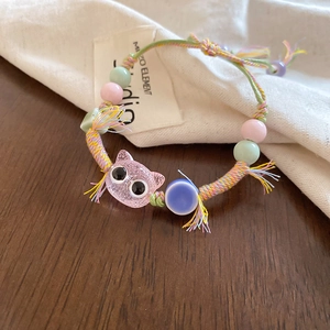 Macro shot of handmade woven bracelet featuring pink glitter cat charm and pastel beads