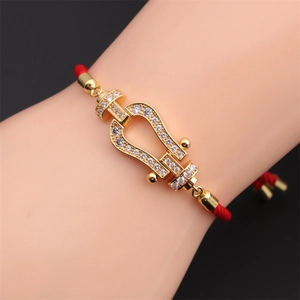 Detail of red braided rope bracelet with gold horseshoe buckle and zircon inlay