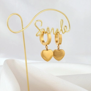 Close-up of golden heart pendant earrings hanging on a smile stand over white silk fabric