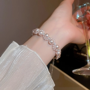 Detailed view of layered pearl bracelet with crystals on a woman's wrist holding a glass