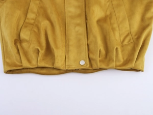 Details einer senfgelben Wildlederjacke mit silbernem Druckknopf und Falten am Saum