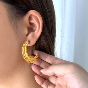 Gros plan de boucles d'oreilles créoles dorées en acier inoxydable à texture ajourée