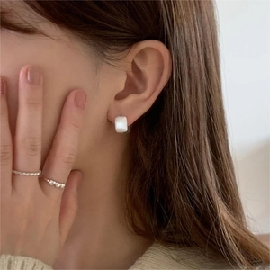 Close-up of elegant square white stud earrings and textured silver rings on a model