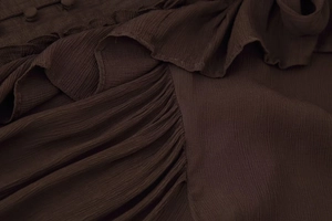 Détail de tissu de chemise marron foncé avec plis élégants, volants et boutons assortis