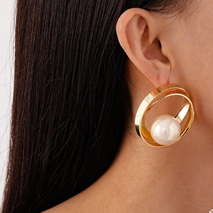 Gros plan de boucles d'oreilles créoles dorées géométriques avec une grande perle blanche