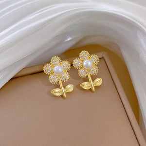 Golden flower earrings with white pearl and sparkling crystals on silk background