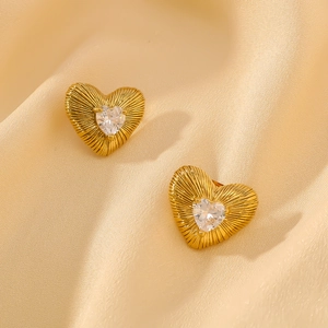 Close-up of gold heart earrings with zircon stones on soft beige satin fabric