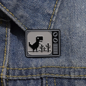 Macro detail of pixel dinosaur enamel pin on blue denim fabric with retro TV frame design