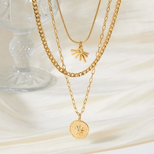 Three-layer gold sun and coin pendant necklace on bamboo chain over white silk fabric