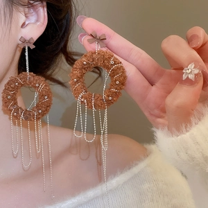 Model wearing brown plush circle earrings with silver tassel fringe and bow decoration