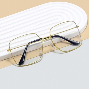 Modern oversized square glasses with gold metal frames and black temples on white stand