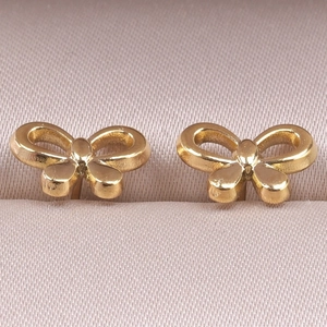 Detailed close-up of golden bow stud earrings on soft pink silk background texture