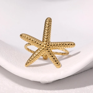 Minimalist gold starfish ring with beaded texture on a white decorative ceramic tray