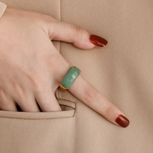 Close-up of a green faceted gemstone ring with gold band styled on a beige blazer pocket