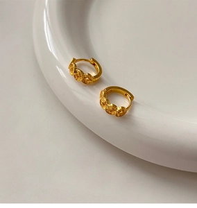 Close-up of 18k gold plated copper coin vintage hoop earrings on white ceramic plate