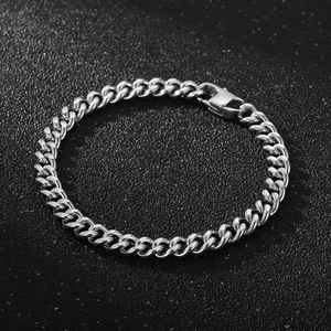 Detail of silver Cuban link bracelet with lobster clasp on a black textured surface