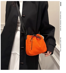 Close-up of bright orange nylon drawstring bucket bag on model with black strap